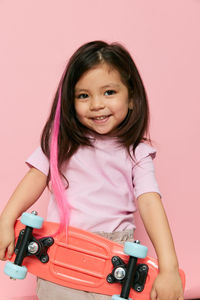 Portrait of young woman holding headphones while standing against pink background