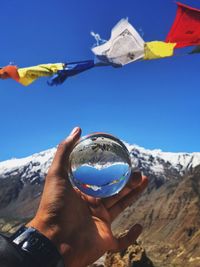 Cropped hand holding crystal ball against snowcapped mountain
