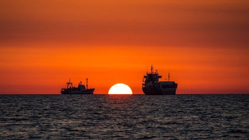 Ship sailing in sea at sunset