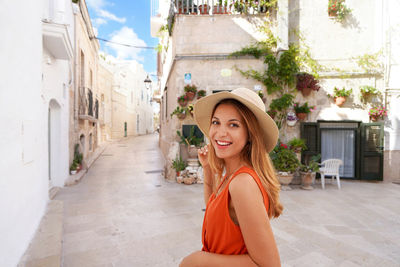 Portrait of young tanned woman with hat and orange dress enjoying her summer holidays in italy.