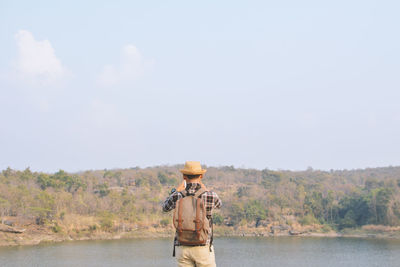 Rear view of man standing on riverbank against sky