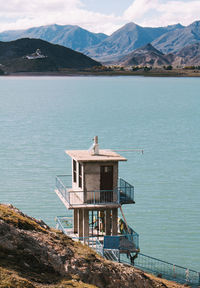 Built structure by sea and mountains against sky