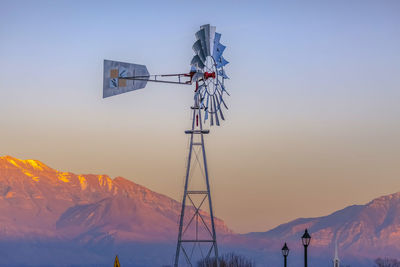 Windmill on snowcapped mountain against sky during sunset