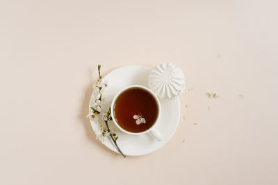 Cup of black tea with marshmallows and spring flowers of apple tree on beige background
