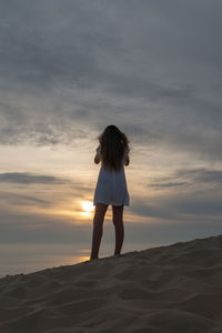 Woman standing on beach against sky during sunset