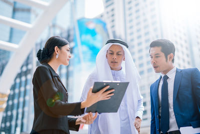 Business colleagues looking at clipboard while standing against buildings in city