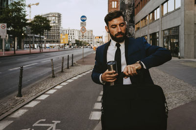 Male entrepreneur checking time while standing on footpath
