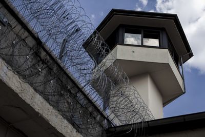 Low angle view of lookout tower by barbed wire fence against sky