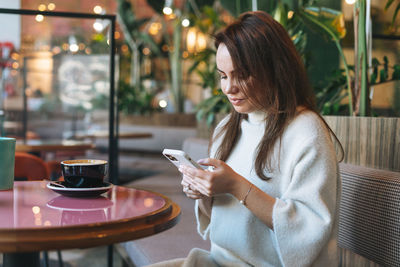 Midsection of woman holding coffee while sitting on table at cafe