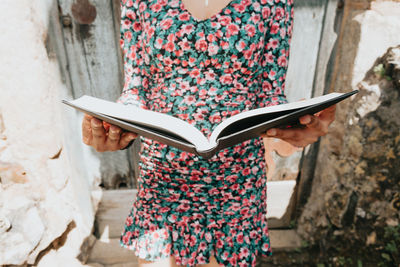 Midsection of woman holding book against wall