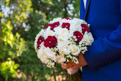 Midsection of bridegroom holding rose bouquet