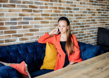 A young woman is sitting on a soft sofa and talking on the phone. stylish youth image.