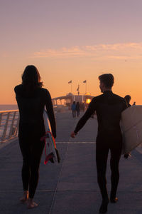 Rear view of friends standing against sea during sunset