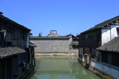 Canal by houses against clear blue sky