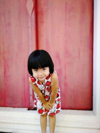 Portrait of girl standing against closed red door