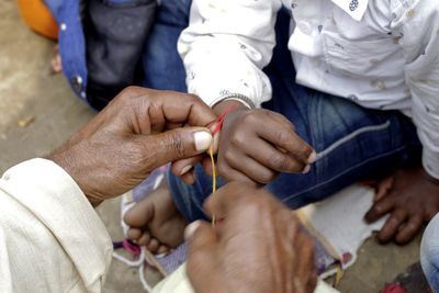 Close-up of man tying thread on boy hand