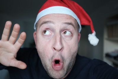 Close-up of shocked man wearing santa hat at home