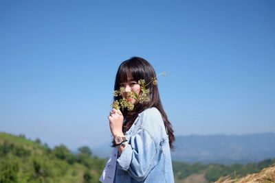 Portrait of woman holding flower against clear sky