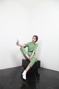 Teenage girl using phone standing against wall