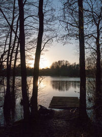 Silhouette trees by lake against sky at sunset