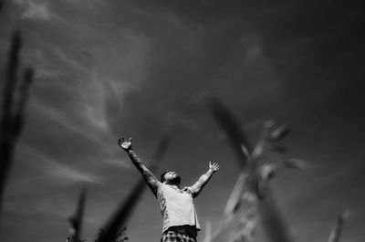 Low angle view of young man with arms raised while standing against sky