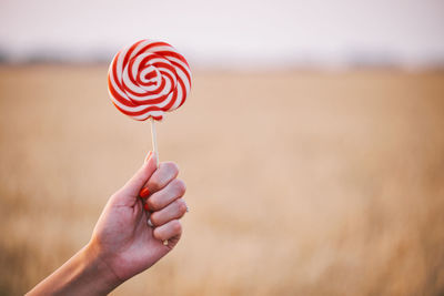 Close-up of hand holding red lollipop on field