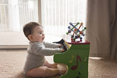 Side view of curious baby boy playing toy piano at home