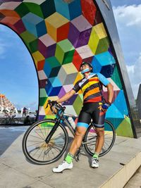 Low section of man with bicycle standing on multi colored umbrella