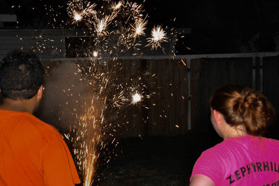 Rear view of people looking at illuminated firework at night