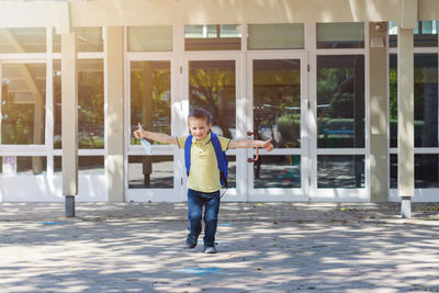 Boy wearing a protective mask with a backpack behind his back in the schoolyard on the first school 