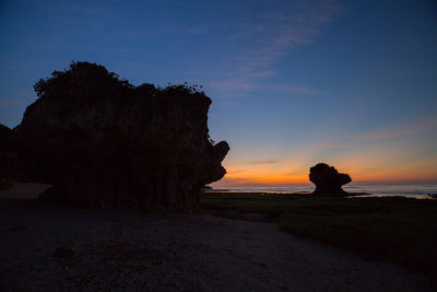 Silhouette rock formation on beach against sky during sunset