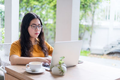 Young woman using phone while sitting on table