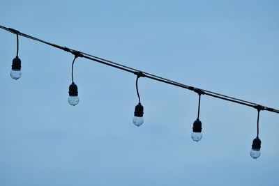 Low angle view of light bulbs hanging against clear sky