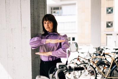 Portrait of young woman gesturing equal sign while standing by bicycle and wall