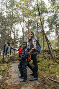 Side view of smiling woman standing on trail with son in forest during vacation