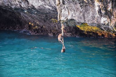 Full length of shirtless man on rock in sea