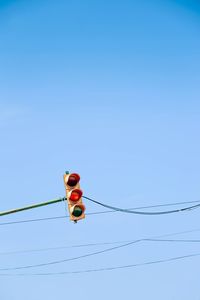 Low angle view of road signal on cables against clear blue sky