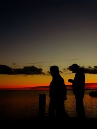 Silhouette people on beach against sky during sunset