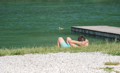 Shirtless man lying on grass by lake 