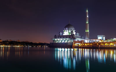 Illuminated mosque by sea against sky at night