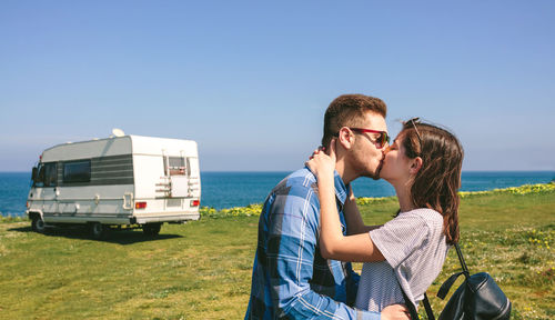 Side view of couple kissing on shore against clear blue sky