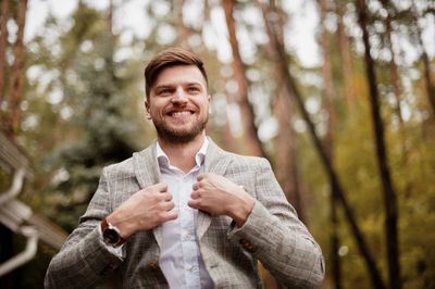 Low angle view of businessman smiling while standing against trees