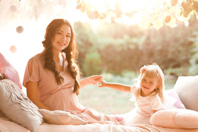 Portrait of mother and daughter sitting on bed