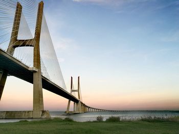 Suspension bridge over sea against sky during sunset