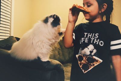 Girl holding pizza while standing by cat at home