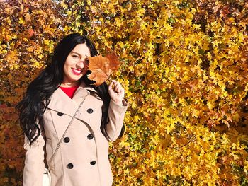 Smiling young woman standing with yellow autumn leaves