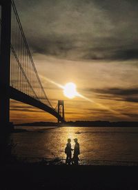 Silhouette of suspension bridge over river during sunset