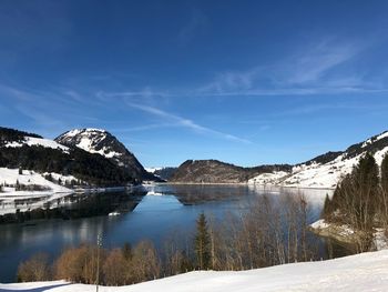 Scenic view of lake and snowcapped mountains against blue sky