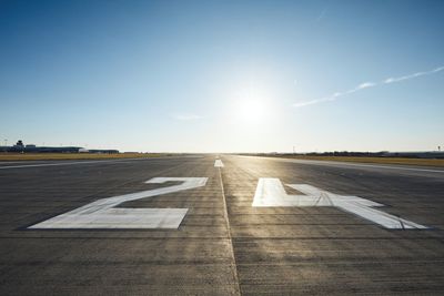 Surface level of airport runway with road marking and number 24 against clear sky.