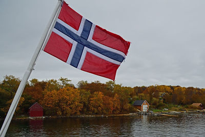 Red flag by lake against sky